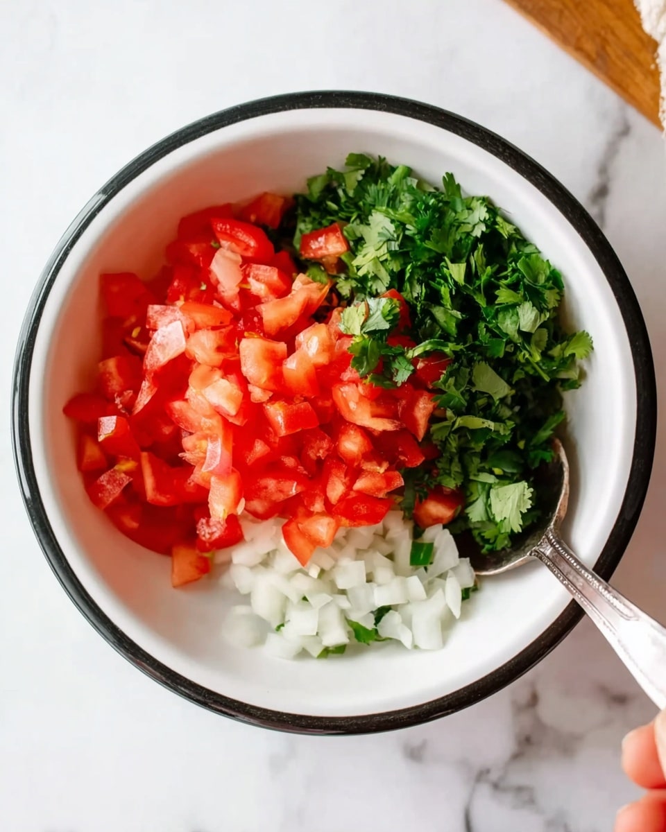 A white bowl with a black rim sits on a white marbled surface, filled with three sections of finely chopped ingredients: bright red tomatoes stacked on the top left, small white onion pieces to the bottom left, and fresh green cilantro leaves with some onion pieces on the right. A woman's hand holding a small metal spoon is partially visible on the right side near the bowl. Photo taken with an iphone --ar 4:5 --v 7