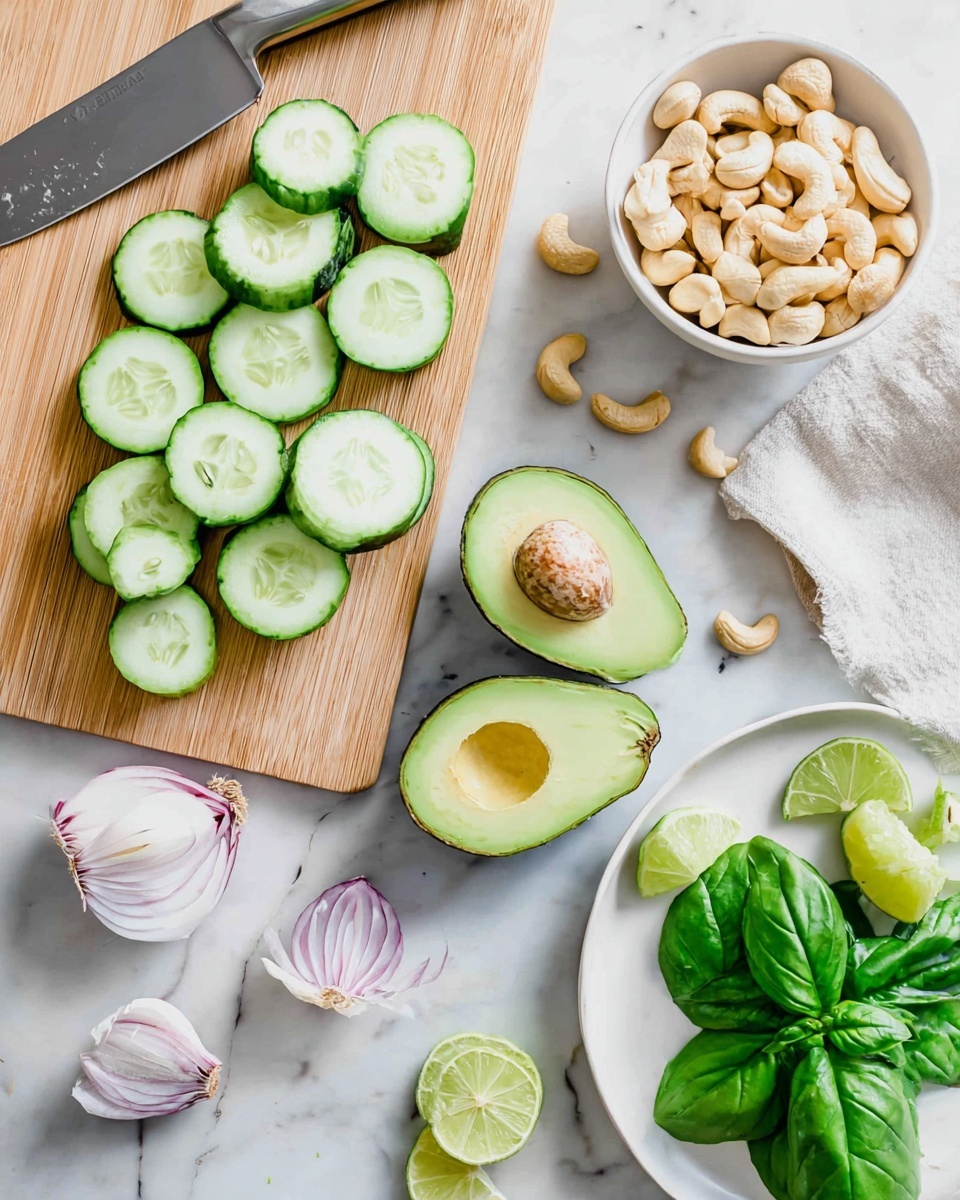 A light wood cutting board centered on a white marbled surface holds a cucumber that is partially sliced into bright green rounds with pale centers arranged in two neat rows, one vertical and one diagonal. To the right, there is a halved avocado with bright green flesh and a large brown seed in one half, and an empty cavity in the other. Nearby, a white bowl filled with pale beige cashew nuts sits next to a halved small red onion with white and light red layers visible. A peeled garlic clove and two lime halves with light green inner flesh lay scattered nearby. A white plate on the lower right corner contains fresh green basil leaves, and a few loose basil sprigs are placed on the marbled surface. A stainless steel knife with a black handle rests above the cutting board. photo taken with an iphone --ar 4:5 --v 7