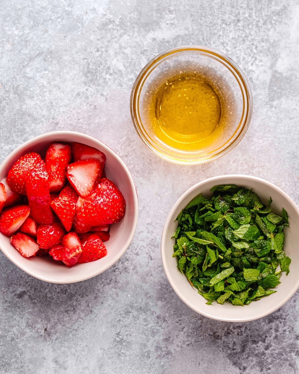 The image shows three small bowls on a white marbled surface. The left bowl is white filled with bright red strawberries, some whole and some sliced, with a juicy texture. In the middle, there is a clear glass bowl with a golden yellow liquid, slightly thick and shiny. The bowl on the right is white and contains chopped green fresh mint leaves with a soft, leafy texture. All bowls are arranged spaced evenly across the surface. photo taken with an iphone --ar 4:5 --v 7
