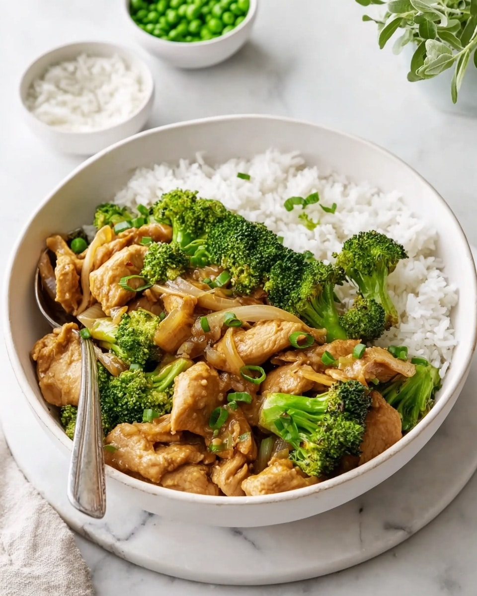 A white bowl filled with a layer of white rice at the bottom. On top of the rice, there is a layer of light brown cooked chicken pieces mixed with browned onion slices and bright green broccoli florets. The chicken pieces have a smooth texture coated with a light sauce. The broccoli is vibrant and fresh looking with a rough texture. A silver spoon is placed in the bowl resting on the side with a white marbled surface beneath it. In the background, there are small white bowls of green peas and white rice, and a green plant. photo taken with an iphone --ar 4:5 --v 7