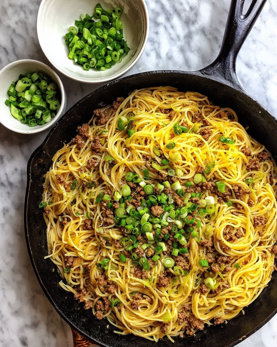 A large black cast iron pan filled with a single layer of cooked thin yellow spaghetti noodles mixed evenly with small brown ground beef pieces, topped with scattered chopped green onions. To the left, a small white bowl holds more chopped green onions, all set on a white marbled textured surface. photo taken with an iphone --ar 4:5 --v 7