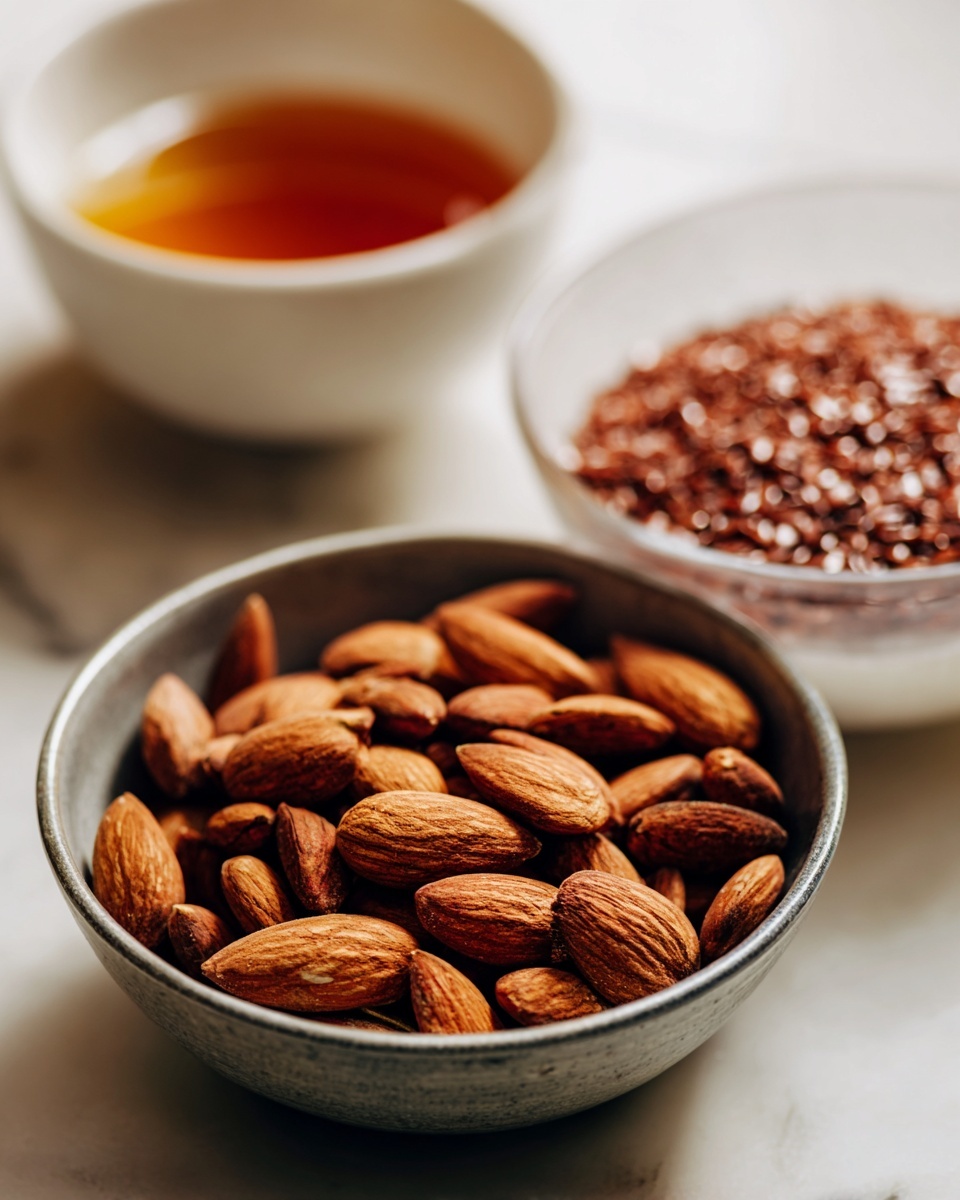 A close-up image shows three bowls placed on a white marbled surface. The main focus is a metal bowl filled with whole almonds, brown with a slight textured skin, almost full and positioned on the left side. To the right, there is a clear white bowl filled with reddish-brown flax seeds that are small, shiny, and smooth. Behind the flax seeds, there is a white bowl holding dark amber liquid, likely honey, visible at the top edge. The background is softly blurred, highlighting the bowls and their contents. Photo taken with an iphone --ar 4:5 --v 7