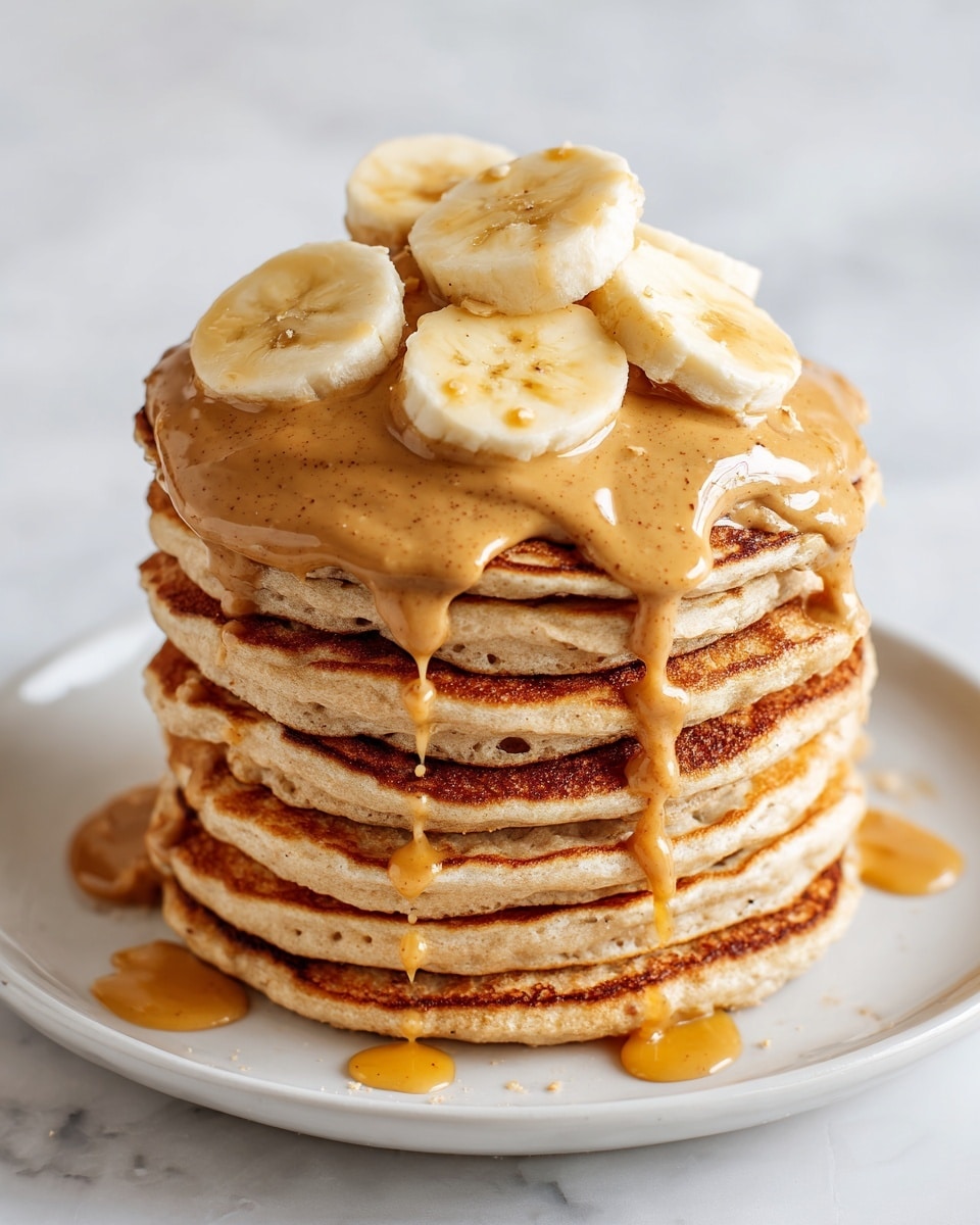 A tall stack of seven golden-brown pancakes with slightly darker edges sits on a white plate on a white marbled surface. The top pancake is covered with a thick drizzle of light brown nut butter spread unevenly, with glossy honey hanging off the sides and pooling on the surface below the stack. On top of the nut butter are six thick, pale yellow banana slices arranged in a loose, neat cluster. The texture of the pancakes looks fluffy and soft with small air bubbles visible. photo taken with an iphone --ar 4:5 --v 7