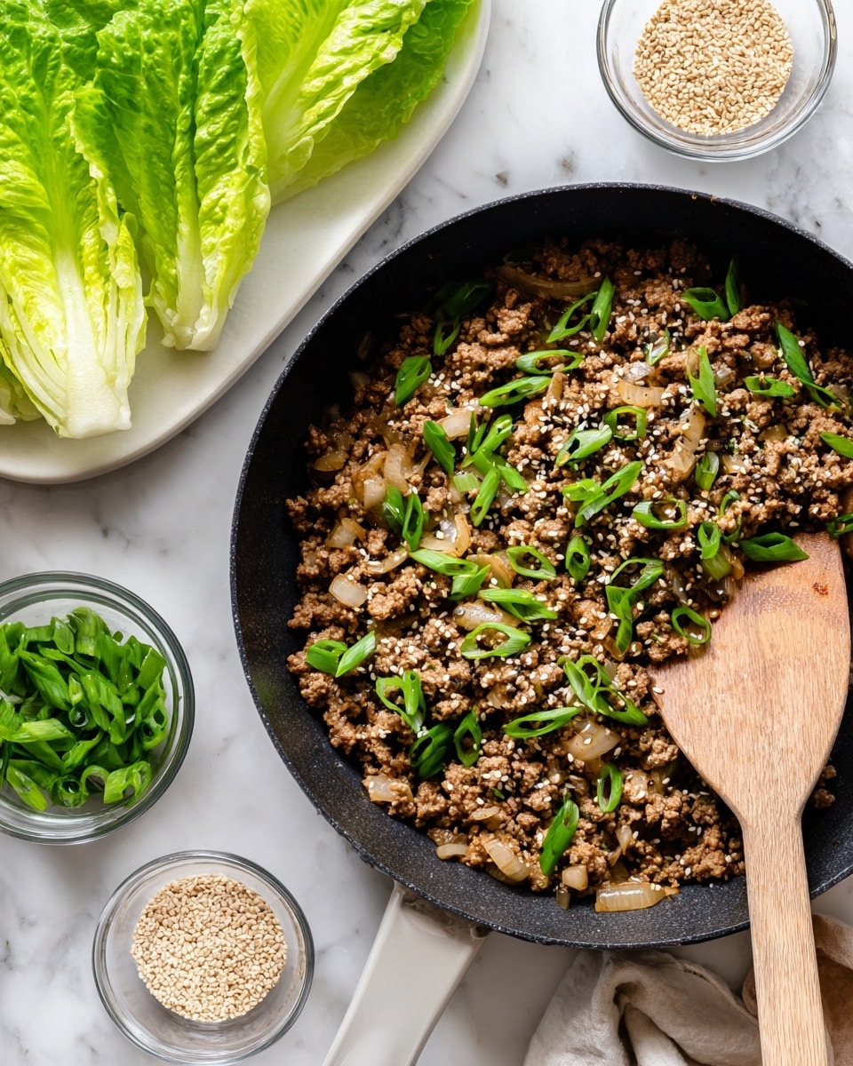 The image shows a close-up of a black pan filled with cooked ground meat mixed with small light brown onion pieces, garnished with bright green sliced spring onions and sprinkled with white sesame seeds and black pepper. A wooden spoon with a light handle is resting inside the pan, partially covered by the food. Around the pan, on a white marbled surface, there are small clear bowls with sesame seeds and chopped green onions, and a white plate holding large fresh green lettuce leaves. Photo taken with an iphone --ar 4:5 --v 7