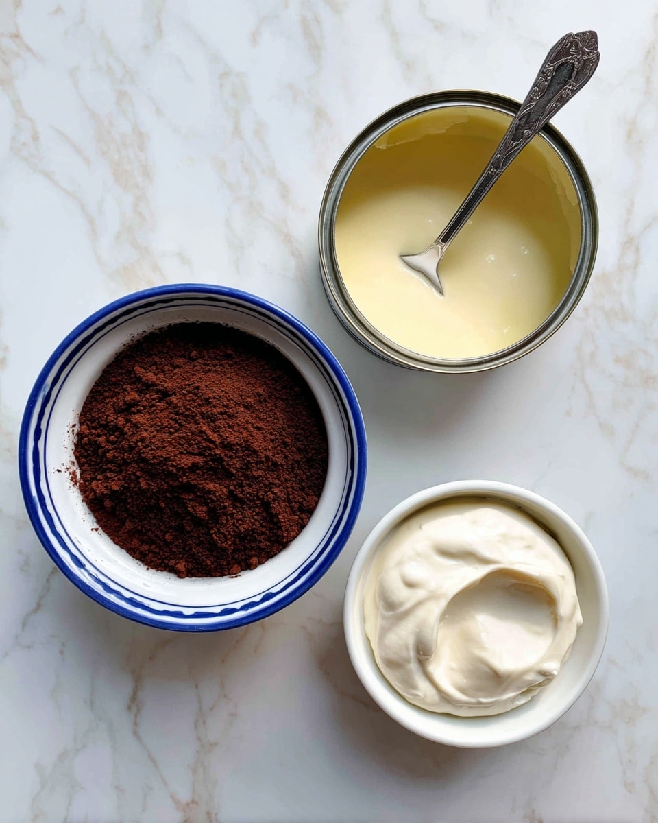 The image shows three items arranged on a white marbled surface: a white bowl with a blue inner rim filled with dark brown cocoa powder that has a slightly clumpy texture, a silver can partially open with a smooth, pale yellow creamy liquid inside and a spoon resting in it, and a small white bowl containing a thick, smooth white cream. Photo taken with an iphone --ar 4:5 --v 7