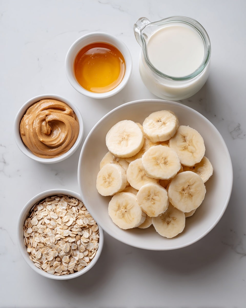 The image shows several white dishes arranged on a white marbled surface. In the center is a white bowl filled with many round banana slices, pale yellow with light brown centers, stacked roughly flat. To the top right is a clear glass jug filled with white milk. Below the jug and to the right is a small white bowl with smooth, light brown peanut butter. Below and to the left of this is another small white bowl filled with pale rolled oats. To the left of the oats, another small white bowl contains golden honey with a shiny surface. All items are evenly spaced around the central bowl of bananas. photo taken with an iphone --ar 4:5 --v 7