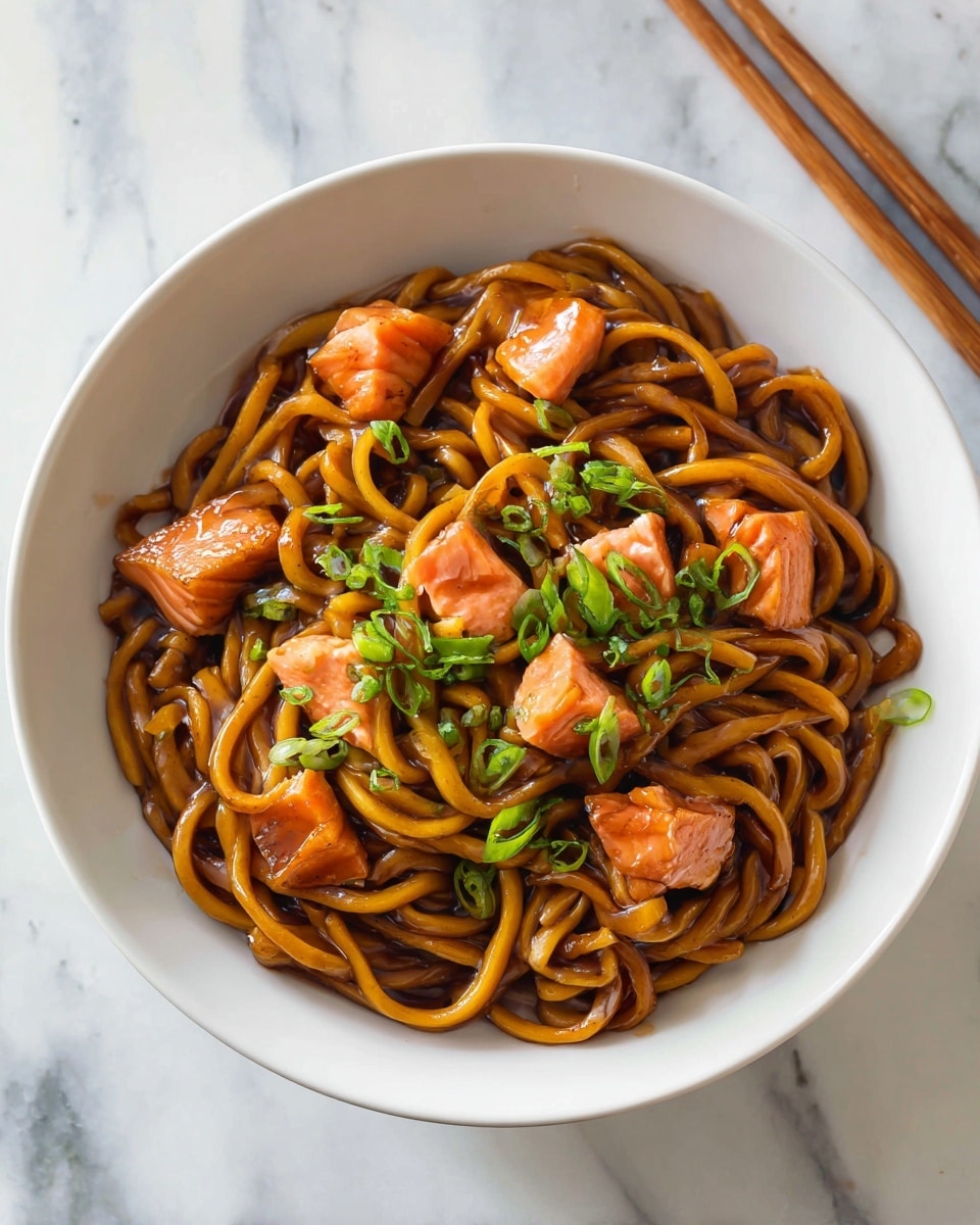 A white bowl holds a serving of thick noodles coated in a glossy brown sauce, twirled into a loose nest shape. On top are several chunks of cooked salmon with a soft coral color, scattered evenly. Small green onion slices are placed over the noodles and fish, adding a fresh green contrast. The bowl sits on a white marbled surface with a pair of chopsticks resting in the background. photo taken with an iphone --ar 4:5 --v 7
