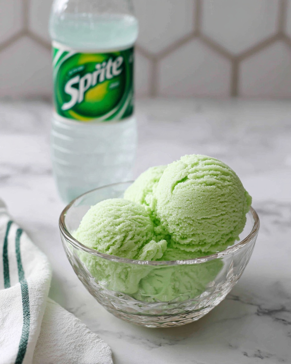 A clear glass bowl sits on a white marbled surface with a hexagon tile pattern, filled with bright pale green scoops of a soft, fluffy textured mixture. Behind the bowl, there is a clear plastic bottle of Sprite with a green and white label. A white cloth with thin green stripes is partially visible at the bottom left corner. The overall scene is clean and simple with soft lighting. photo taken with an iphone --ar 4:5 --v 7