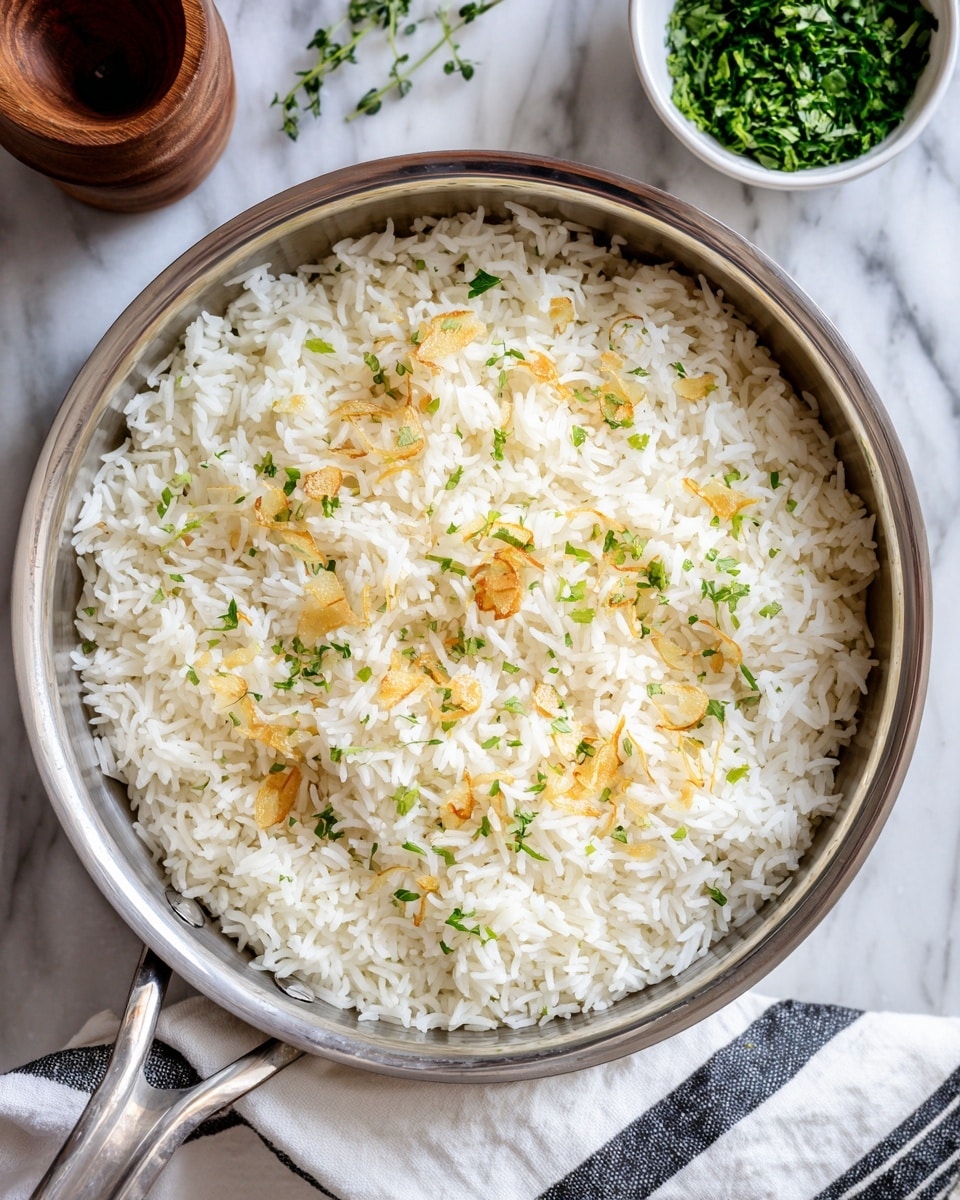 The image shows a single layer of fluffy white rice inside a silver pan. The rice is evenly spread, with light golden, thin garlic slices scattered on top. Small green herb pieces are sparsely sprinkled over the rice, adding a touch of color. The pan rests on a white marbled surface, with a white bowl of more chopped green herbs and a wooden container nearby, along with a white cloth with black stripes on the side. photo taken with an iphone --ar 4:5 --v 7