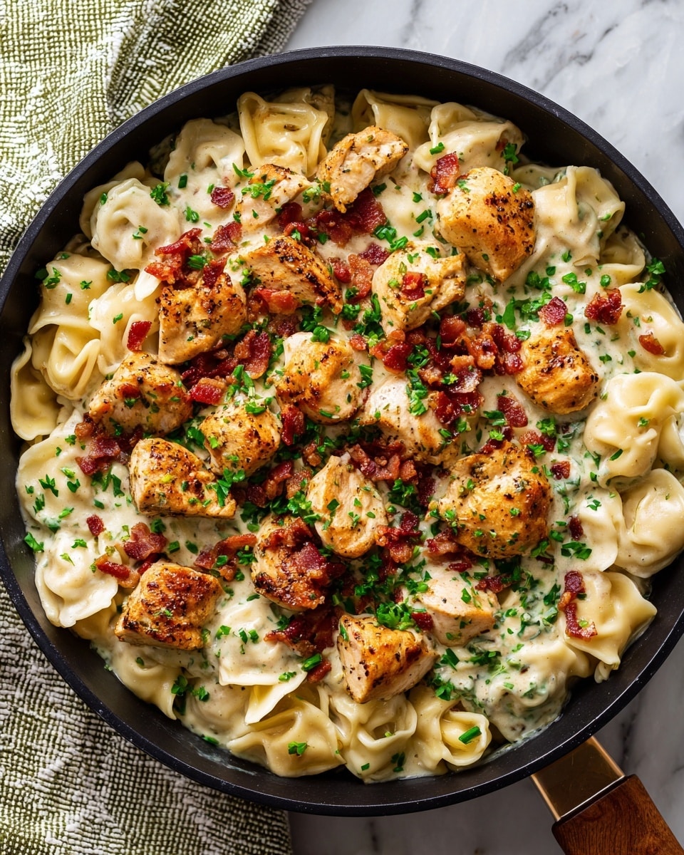 A close-up view of a skillet filled with a creamy pasta dish featuring three main layers: the bottom layer is smooth white pasta with a soft, folded shape; the middle layer consists of several pieces of golden-brown, seasoned cooked chicken chunks scattered on top; and the top layer shows small bright green chopped herbs sprinkled evenly along with pieces of crispy red bacon. The skillet is black and sits on a white marbled surface with a textured white and green cloth nearby. The colors include warm browns, creamy whites, bright green, and a hint of red, with clear details on the texture of the chicken and pasta photo taken with an iphone --ar 4:5 --v 7