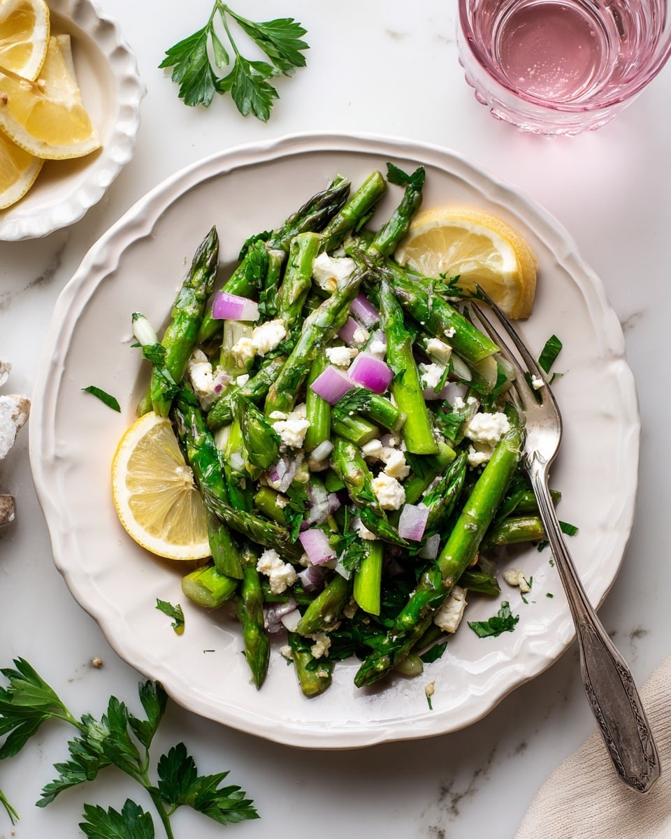 A white carved plate holds a fresh salad with bright green asparagus cut into pieces, mixed with small cubes of purple onion and white crumbled cheese scattered on top. Two thin lemon slices sit on the edge of the salad, with a few green parsley leaves for garnish. A silver fork rests on the side of the plate. The plate is set on a white marbled surface, with a pink glass of water and a small white dish with lemon slices in the background, along with some green parsley leaves scattered nearby. Photo taken with an iphone --ar 4:5 --v 7